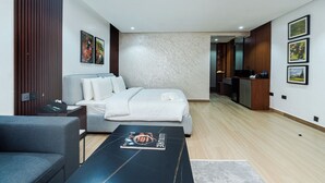 A modern hotel room with a bed, a sofa, a coffee table with a magazine, and a desk with a computer.