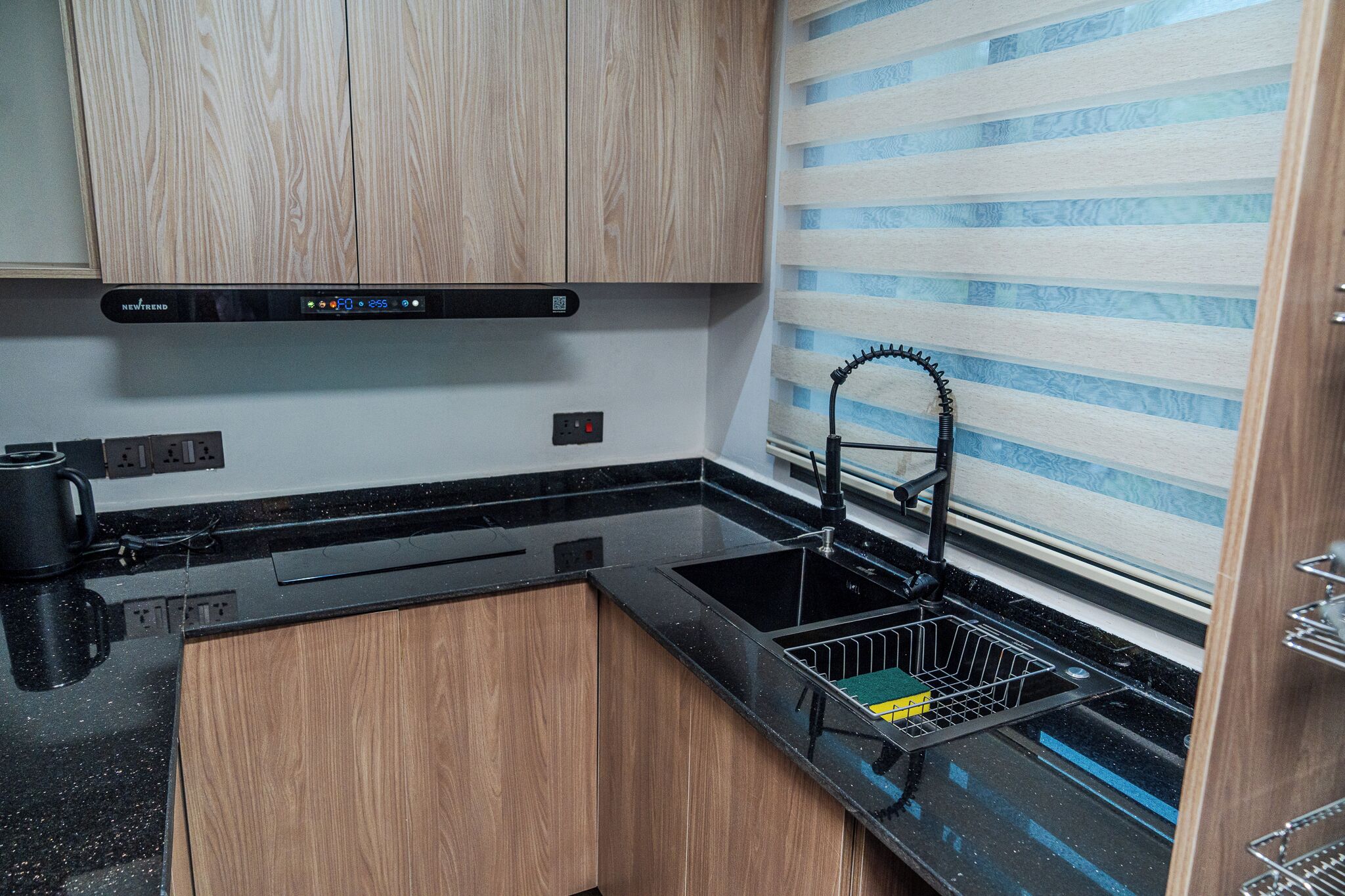 A compact kitchen with wooden cabinets, a black countertop, a stainless steel sink, and a striped backsplash.