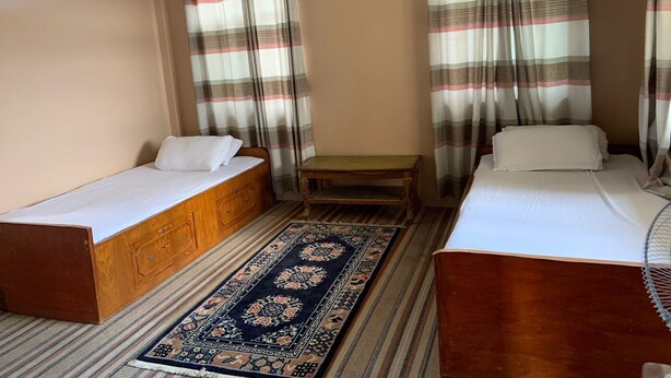 A room with two single beds, a small wooden table, and a patterned rug.