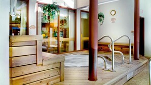 Eine hölzerne Bank und ein Metallstuhl in einer Wellness-Umgebung mit Glastüren und Holzboden.