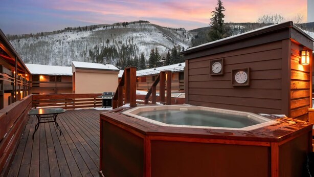 Eine Holzterrasse mit Whirlpool, Holzblockhäusern und Bergblick.