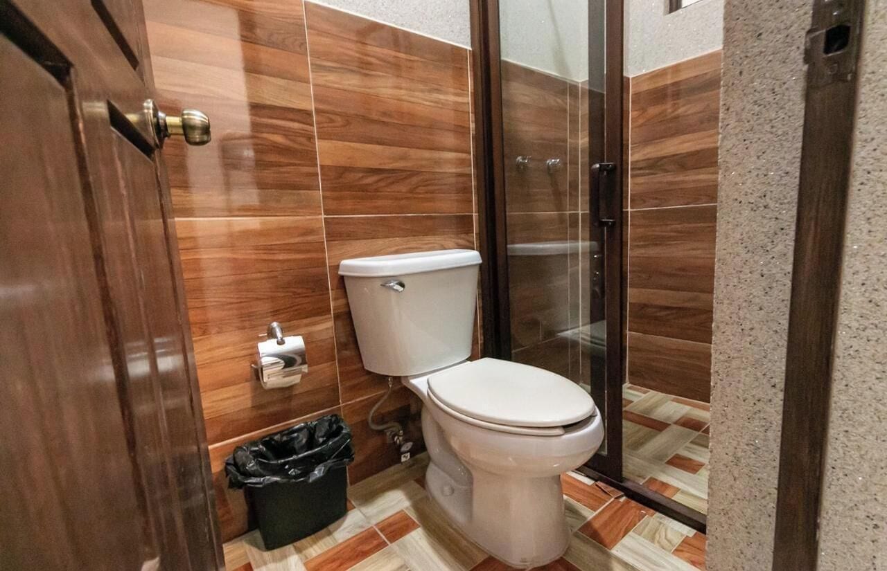 A bathroom with a toilet, a trash bin, and a shower area.