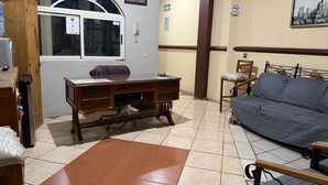 Una habitación con un escritorio de madera, un sofá, una ventana con vistas y una puerta.