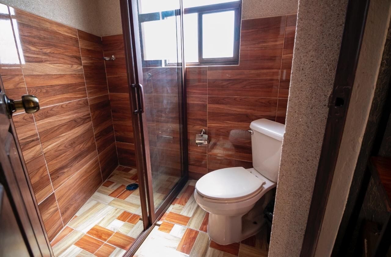 A bathroom with a glass shower enclosure, a toilet, and a tiled floor.