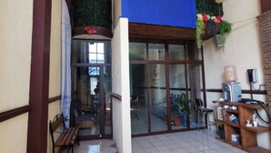 Un suelo de baldosas con un banco, un estante de madera con objetos, y una puerta de cristal que da a un espacio interior.