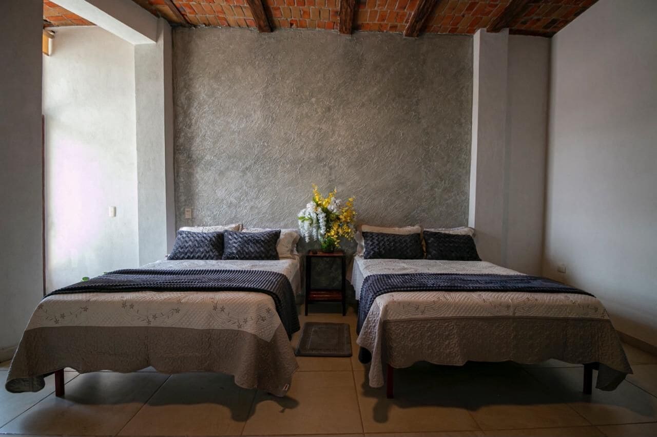 A bedroom with two beds, a small table with a vase of flowers, and a brick ceiling.