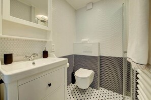 A bathroom with a white sink, a mirror, a toilet, and a shower area. - 1-Bedroom Apartment with a Glass Roof, Downtown (Luxembourg)