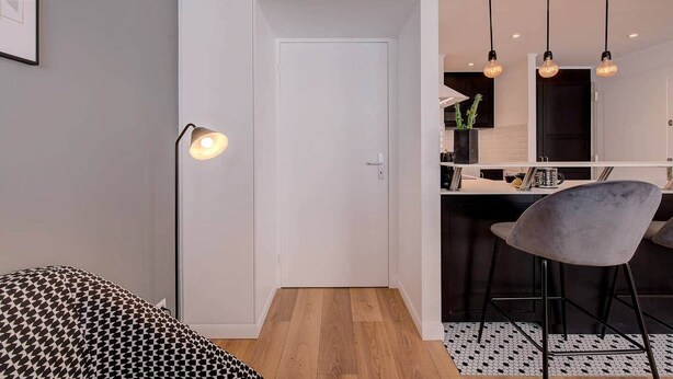 A modern room with a white door, a patterned sofa, a bar area with a grey chair, and pendant lighting. - 1-bedroom apartment with glass roof, city center (Luxembourg)
