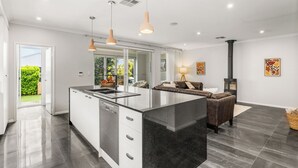A modern kitchen with a central island, a dining area with a sofa, and a fireplace. - Modern Beach Retreat | Eden Beach Sanctuary (Jindalee)