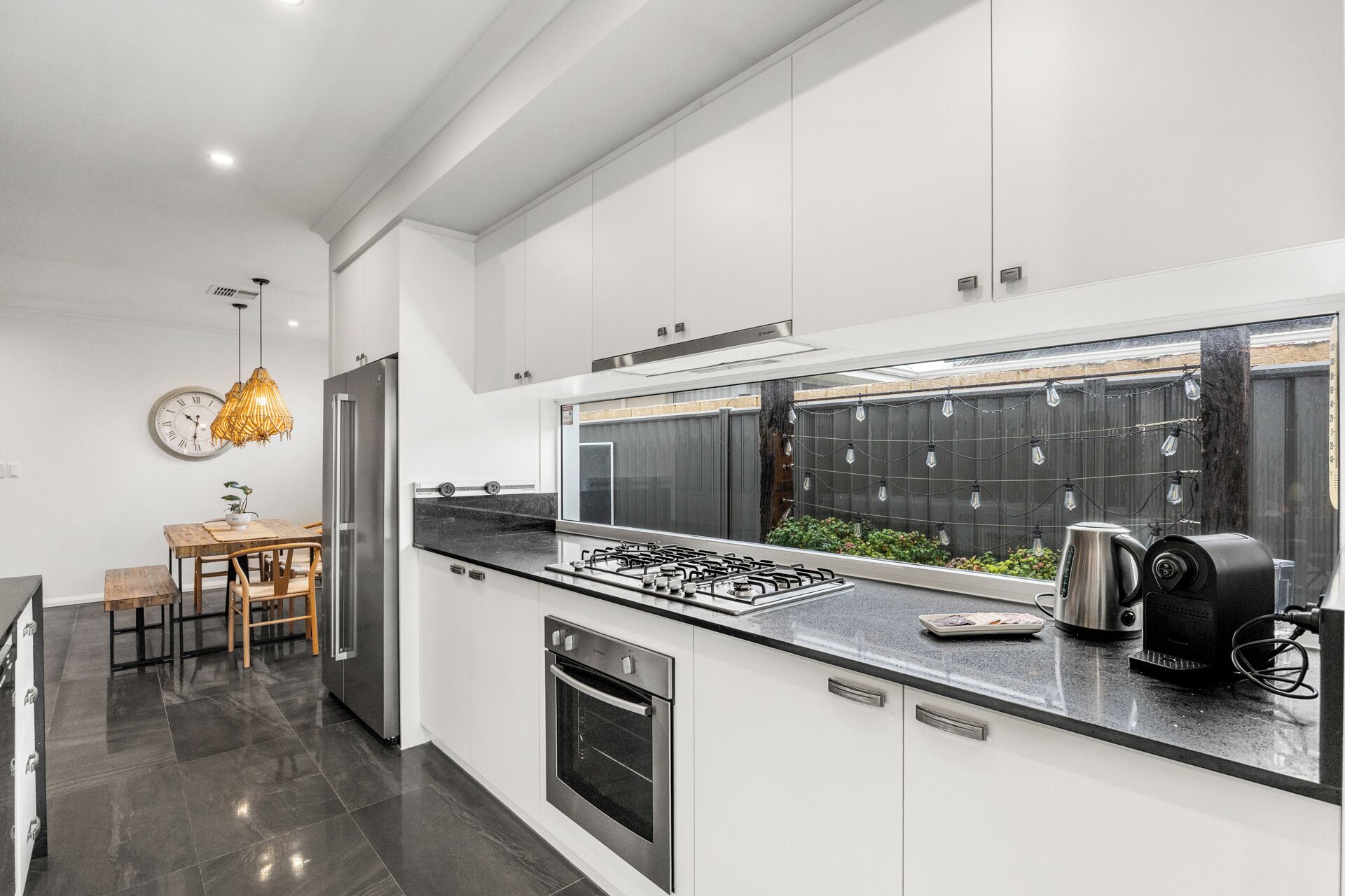 A modern kitchen with white cabinets, a stainless steel refrigerator, a gas stove, and a coffee maker.