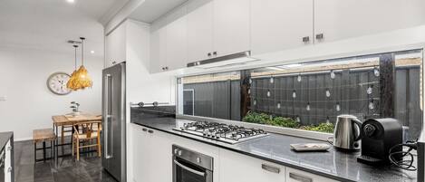 A modern kitchen with white cabinets, a stainless steel refrigerator, a gas stove, and a coffee maker.