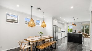 A modern kitchen with a central island, stainless steel appliances, and pendant lighting. - Modern Beach Retreat | Eden Beach Sanctuary (Jindalee)