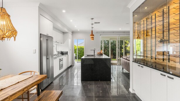 A modern kitchen with a central island, stainless steel appliances, and a dining area with a wooden table and bench. - Modern Beach Retreat | Eden Beach Sanctuary (Jindalee)