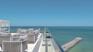 Una terraza en la azotea con mobiliario de mimbre blanco y barandilla de cristal con vistas al mar.