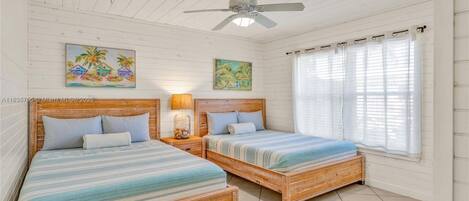 A bedroom with two wooden beds, a ceiling fan, and two paintings on the walls.