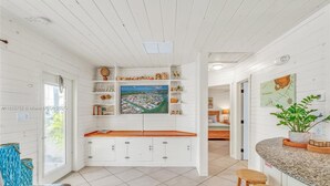 Una cocina amplia con armarios blancos, una isla grande con taburetes y vistas a un pueblo costero a través de una ventana.