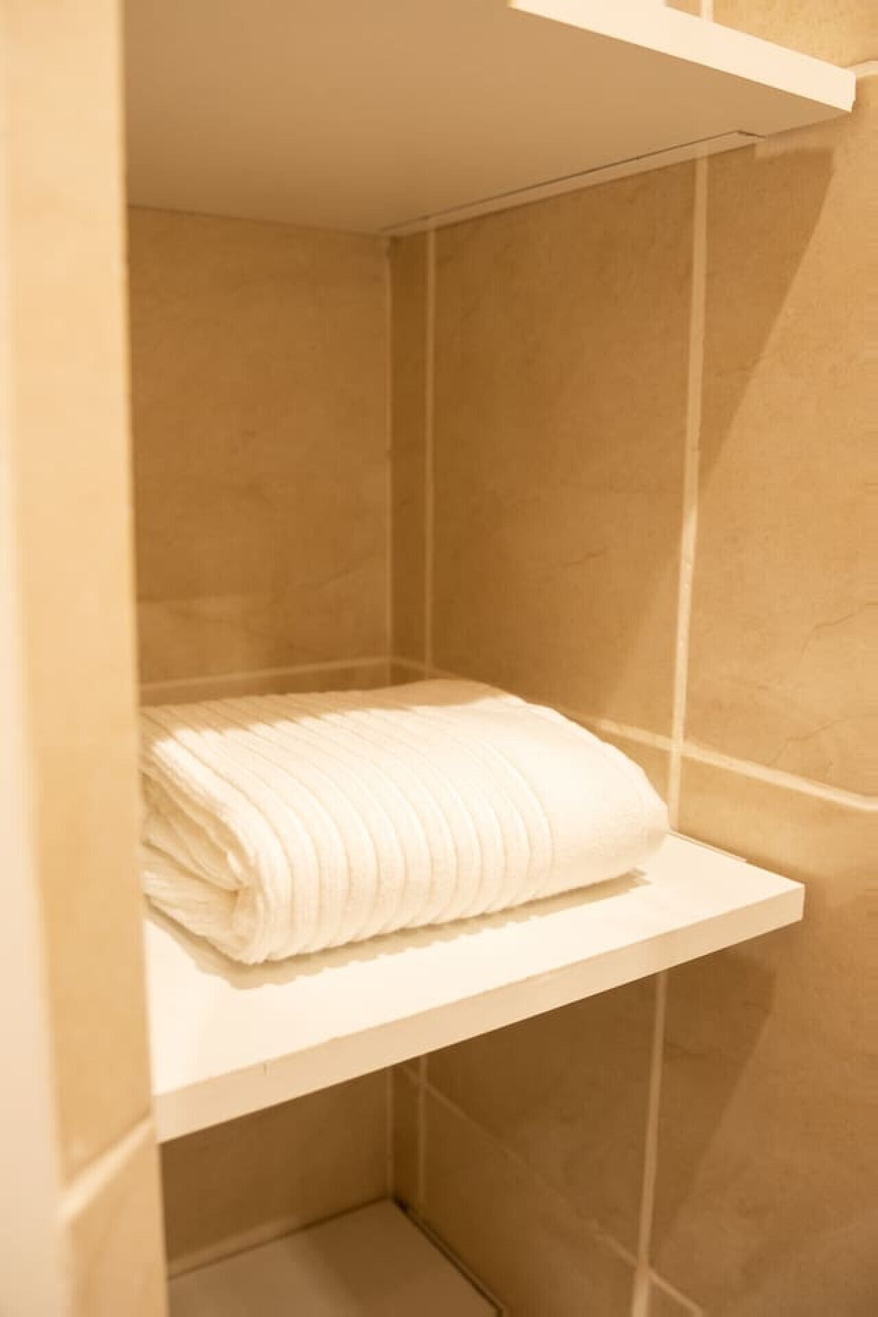 Pequeño espacio de ducha cerrado, con un estante blanco que sostiene una toalla blanca doblada.