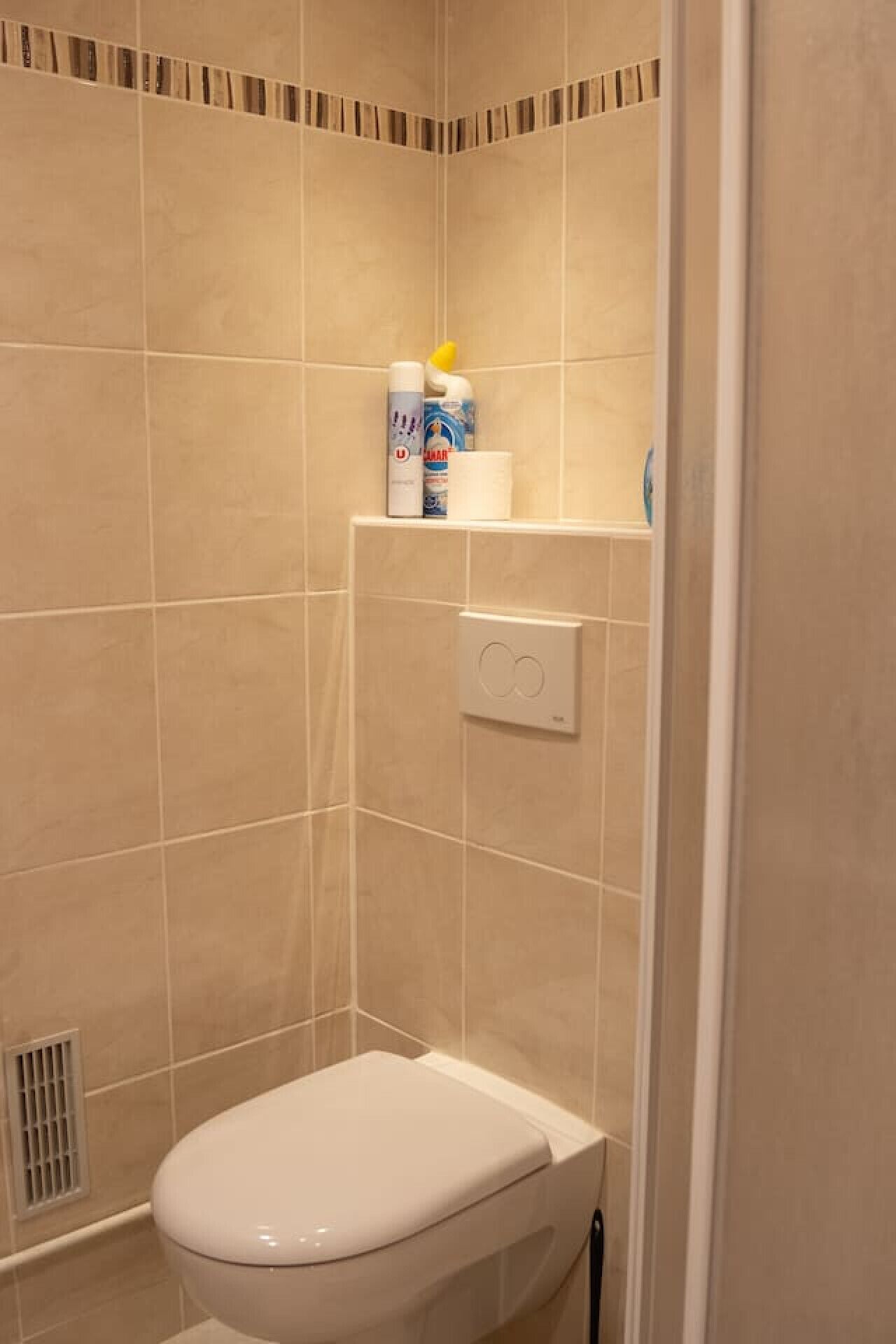A small, enclosed shower stall with a toilet, a shelf with toiletries, and a control panel.