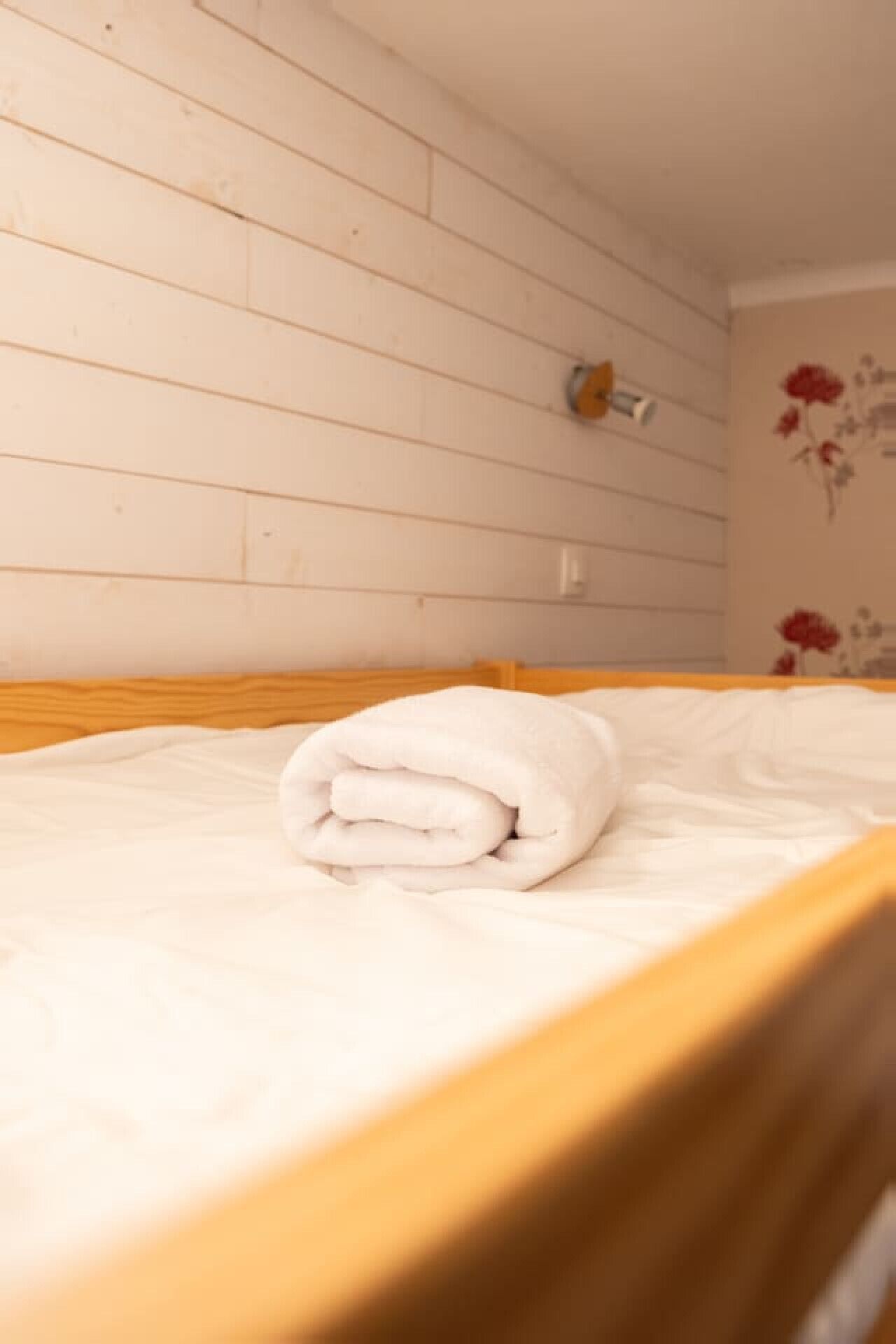 A neatly made bed with a folded white blanket in a room with wooden panel walls and a floral wall decoration.