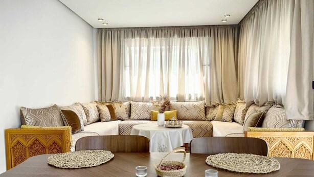 Een moderne woonkamer met een grote L-vormige bank, een eettafel met placemats en een decoratief middelpunt.
