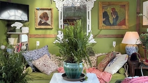 A cozy room with a green wall, a vintage mirror, a green sofa, and a white table.