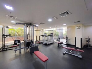 Ein Fitnessraum mit unterschiedlichen Trainingsgeräten, großen Fenstern und einer Bank.