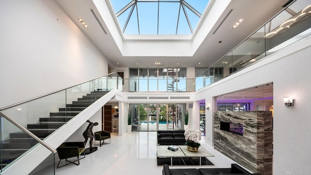 A spacious, modern interior with a high ceiling, a glass staircase, and a central seating area with a marble accent wall. - Luxury 7BR Waterfront Villa w/ Rooftop, Pool & Dock – Sleeps 14 near Las Olas (Fort Lauderdale)