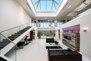Un intérieur spacieux et moderne, doté d’un plafond haut, d’un escalier en verre et d’un espace salon central agrémenté d’un mur décoratif en marbre.