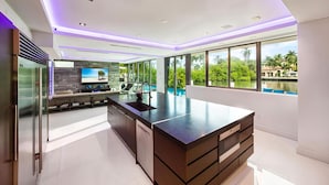 A modern kitchen with a large island, built-in appliances, and large windows offering a view of greenery and water. - Luxury 7BR Waterfront Villa w/ Rooftop, Pool & Dock – Sleeps 14 near Las Olas (Fort Lauderdale)