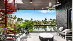 A modern outdoor lounge area with a pool, seating, and a view of palm trees and buildings. - Luxury 7BR Waterfront Villa w/ Rooftop, Pool & Dock – Sleeps 14 near Las Olas (Fort Lauderdale)