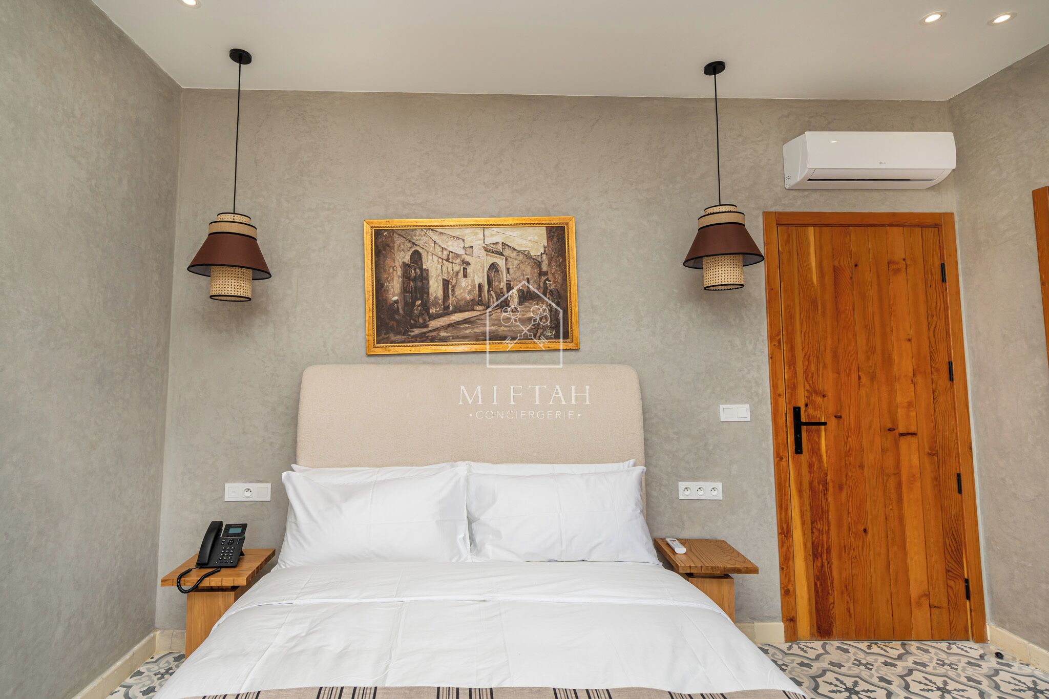 A neatly arranged hotel room with a bed, bedside table, and a painting on the wall.