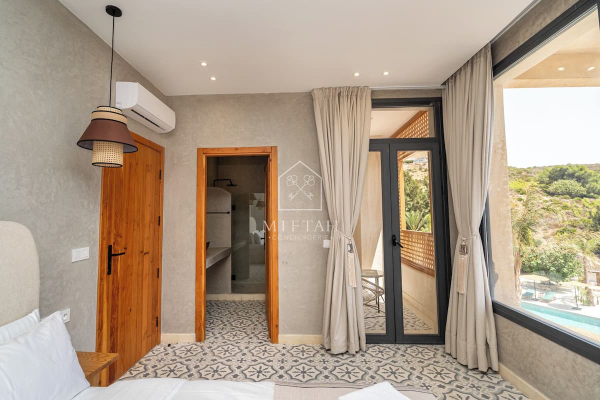 Un dormitorio con cama, un armario de madera, una lámpara colgante y vistas a una piscina y vegetación exterior.