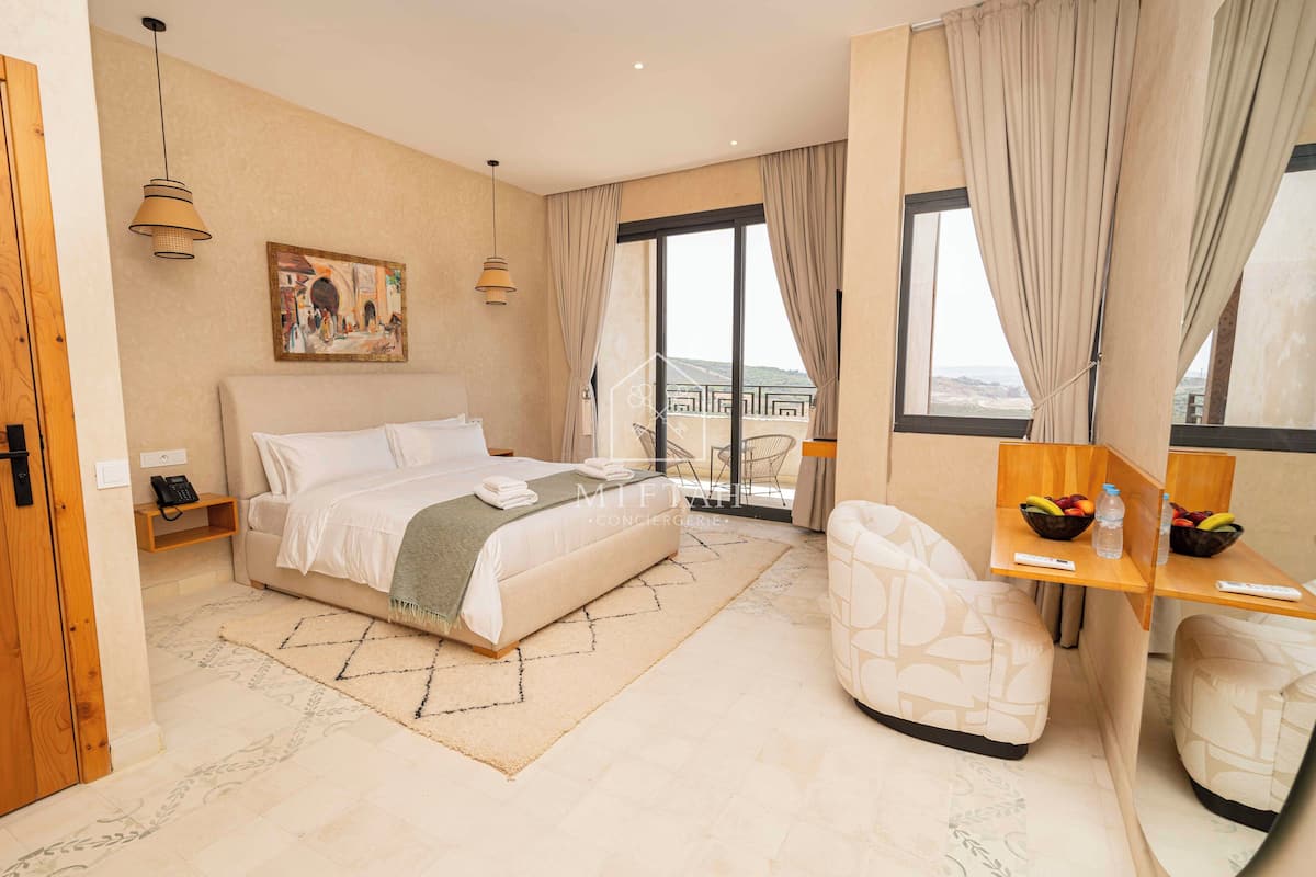 Habitación de hotel moderna con una cama grande, un escritorio con frutero y vistas al exterior.