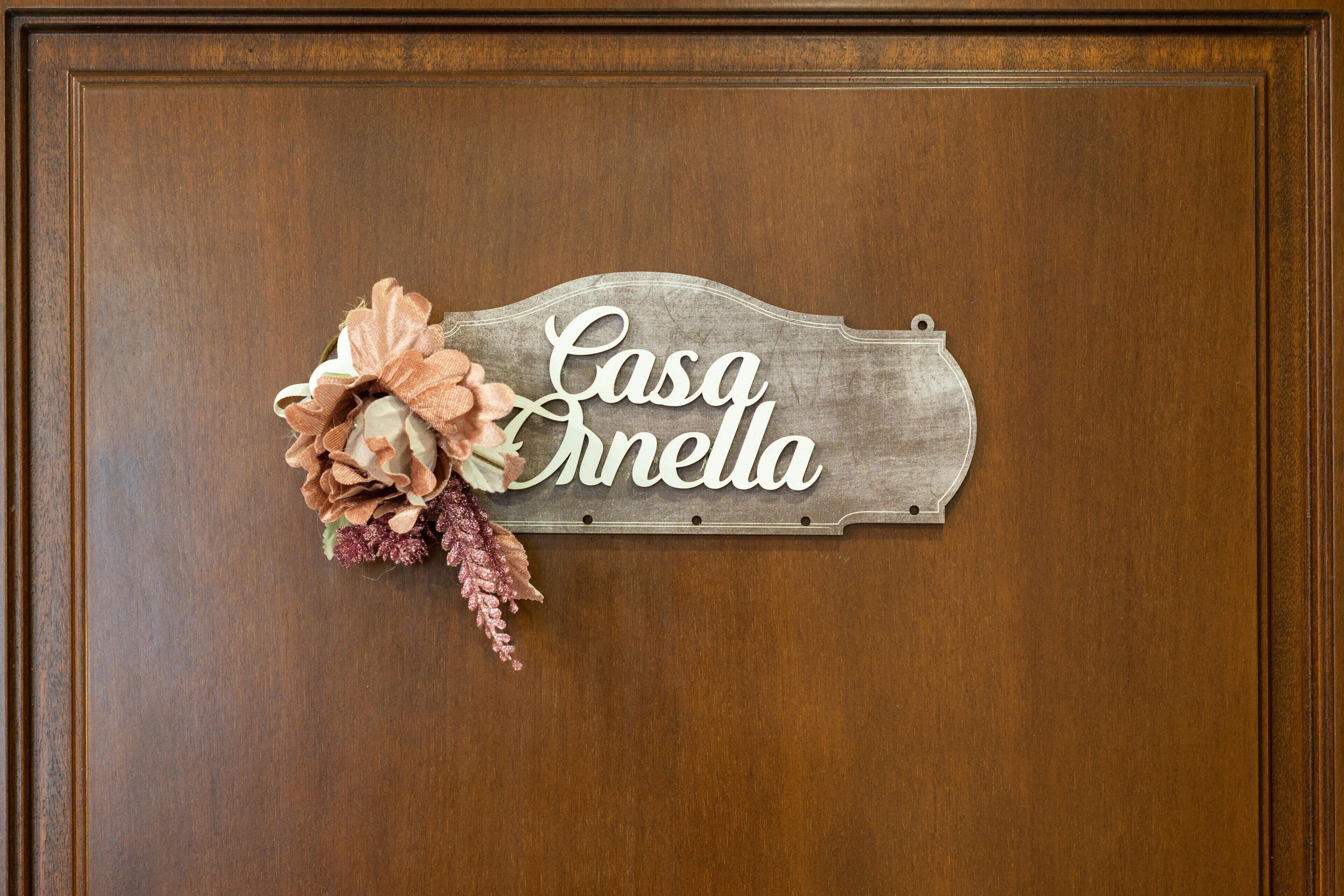 Een houten deur met een bord waarop 'Casa Cinella' staat en een decoratieve bloemstuk.