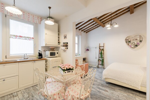 A compact kitchen with a dining table, chairs, and a bed in the adjacent room.