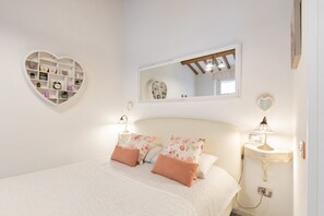 A bedroom with a heart-shaped shelf, a bed with floral bedding, a bedside lamp, and a mirror on the wall. - Casa Ornella – Romantic Studio in the Heart of Florence (Firenze)