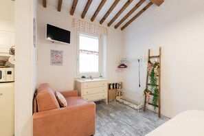 A bedroom with a bed, a dresser, a TV, a window with curtains, a wooden ladder, and a radiator. - Casa Ornella – Romantic Studio in the Heart of Florence (Firenze)