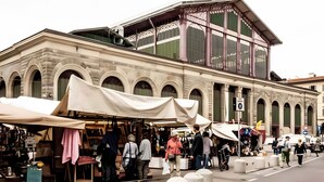 Un edificio histórico con ventanas de arco y una zona de mercado techada al frente.