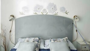 A bed with a grey headboard, white floral wall art, two bedside lamps, and striped bedding. - Casa Ornella – Charm on Two Levels in the Heart of Florence (Firenze FI)