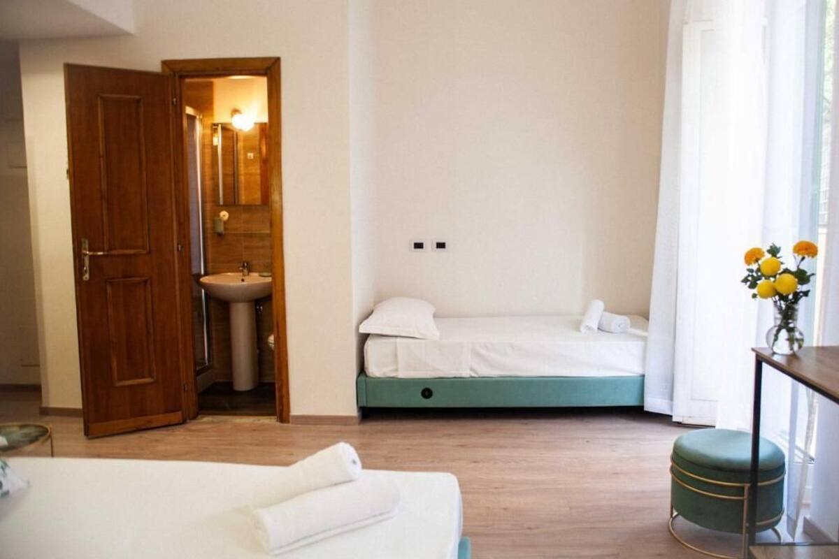 A bedroom with a wooden door, a sink, a bed, and a small table with a vase of flowers.