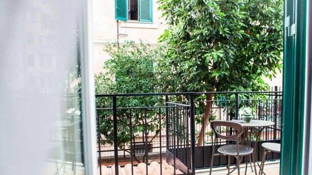A balcony with a metal railing, a table, two chairs, and a potted plant. - Farfalla Bianca - Rooms (Rome)
