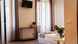 A hotel room with a bed, a bedside table with a vase of flowers, a flat-screen TV mounted on the wall, and a window with curtains. - Farfalla Bianca - Rooms (Rome)
