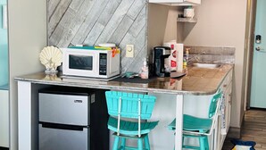 Una cocina compacta con microondas, refrigerador y dos taburetes de bar.
