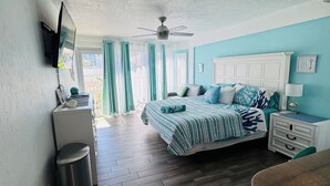 Un dormitorio con cama, ventilador de techo, televisión montada en la pared y ventana con cortinas.