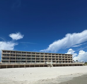 A multi-story hotel with balconies, located on a beach with a clear sky. - Beach Vibes Only (Daytona Beach)