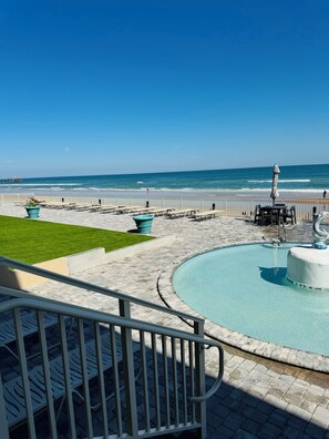 A pool area with a view of the ocean, lounge chairs, and a small fountain. - Beach Vibes Only (Daytona Beach)