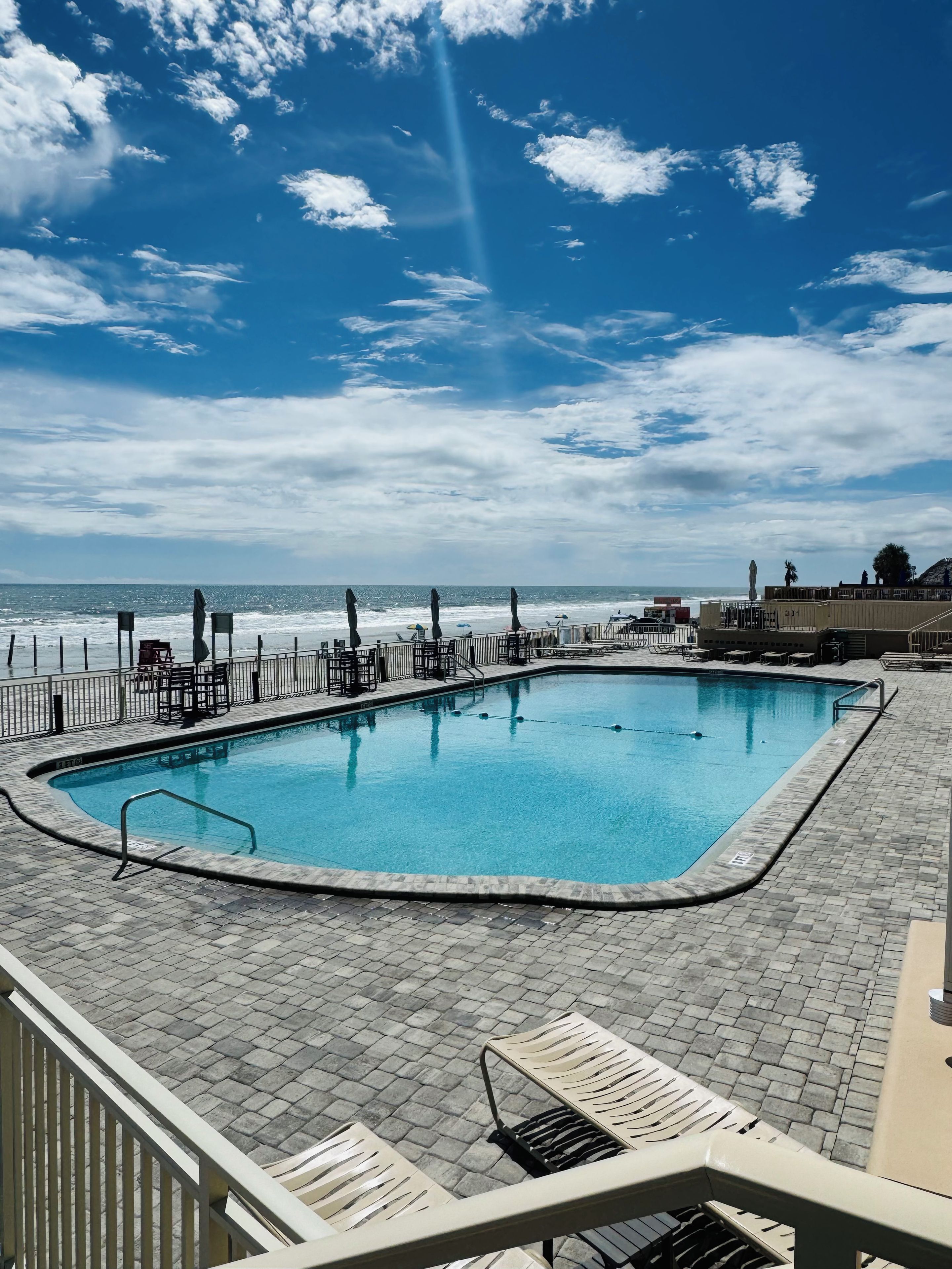 Une piscine avec vue sur l’océan, entourée de chaises longues et d’une clôture.