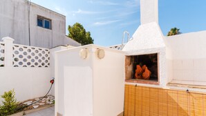 Een witte buitenkeuken met schoorsteen, een klein raam en een slang aangesloten op de muur.