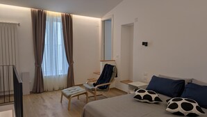 A modern hotel room with a bed, a chair, a small table, and a window with curtains. - The House of Archibugi (Sulmona)