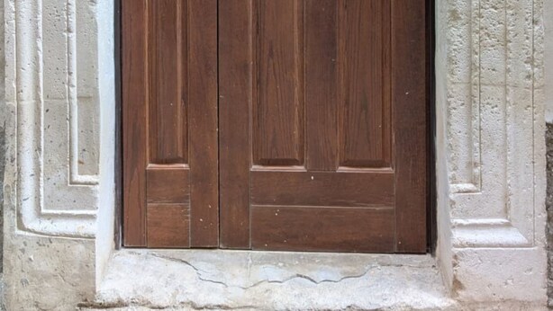 A double wooden door with a brass handle and a brass lock, set in a stone frame with a number '10' above it. - The House of Archibugi (Sulmona)